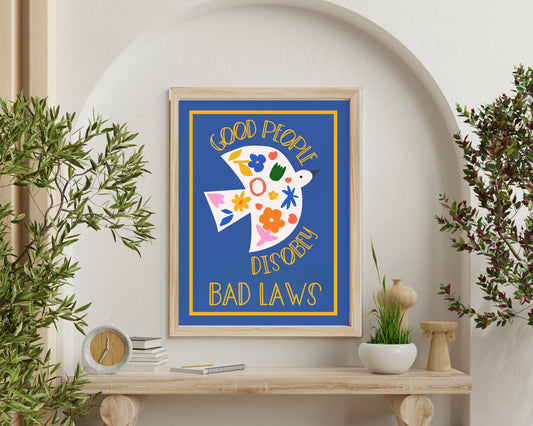 May include: A framed print with a blue background and a white bird with colorful flowers. The text on the print reads &#39;Good People Disobey Bad Laws.&#39;